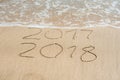 New Year 2018 is coming concept - inscription 2017 and 2018 on a beach sand, the wave is almost covering the digits 2017 Royalty Free Stock Photo