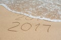 New Year 2017 is coming concept - inscription 2016 and 2017 on a beach sand, the wave is almost covering the digits 2016 Royalty Free Stock Photo