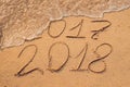 New Year 2018 is coming concept - inscription 2017 and 2018 on a beach sand, the wave is almost covering the digits 2017 Royalty Free Stock Photo