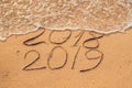 New Year 2019 is coming concept - inscription 2018 and 2019 on a beach sand, the wave is almost covering the digits 2018 Royalty Free Stock Photo