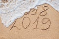 New Year 2019 is coming concept - inscription 2018 and 2019 on a beach sand, the wave is almost covering the digits 2018 Royalty Free Stock Photo