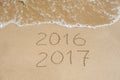 New Year 2017 is coming concept - inscription 2016 and 2017 on a beach sand, the wave is almost covering the digits 2016 Royalty Free Stock Photo