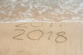 New Year 2018 is coming concept - inscription 2017 and 2018 on a beach sand, the wave is almost covering the digits 2017 Royalty Free Stock Photo
