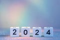 2024 New Year Coming. White Wooden Blocks With 2024 Number On Glitter Texture In Neon Light