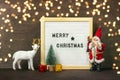 New Year composition of white deer, Santa Claus, lights, tree, gift box, felt board with text Merry Christmas on dark wooden Royalty Free Stock Photo