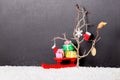 New Year concept of bare tree with mittens, boot, snowflake, Christmas ball and red festive sled, gift boxes in snow on