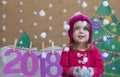 New Year 2018 concept. Beautiful small girl decorating the New Year numeral. background of a painted Christmas tree and