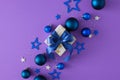 Top view photo of present box with blue bows, Christmas baubles, sequins, stars on violet background Royalty Free Stock Photo