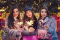 New Year concept. Women friends burning sparklers in Lviv by Christmas tree. Girls holding shopping bags and gifts Royalty Free Stock Photo