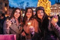 New Year concept. Women friends burning sparklers in Lviv by Christmas tree on street fair. Girls holding shopping bags Royalty Free Stock Photo