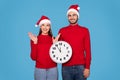 New Year Countdown. Happy Couple In Santa Hats Holding Clock And Smiling