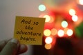 New year inspirational motivational quote on a paper note in hand - And so the adventure begins. On Christmas light background. Royalty Free Stock Photo