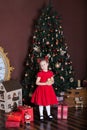 New Year 2020. Merry Christmas, happy holidays. Little girl with a candle in front of a Christmas tree and gifts. New Year decor, Royalty Free Stock Photo