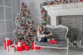 New Year photo session. Young woman on comfortable sofa near Christmas tree with gifts