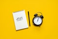 New year resolution, Goals setting for the 2023 year, text 2023 loading in open notepad and alarm clock on yellow desk Royalty Free Stock Photo