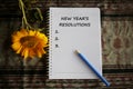 New year resolution list concept on white notebook paper with yellow flower, notebook and pen