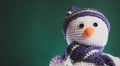 New year\'s card with a handmade toy. Cute knitted white snowman with a carrot for a nose and a striped hat on a green background,