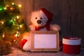 New Year`s, Christmas bear sitting under a fir tree with a wooden frame mockups for a photo or text. Royalty Free Stock Photo
