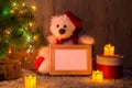 New Year`s, Christmas bear sitting under a fir tree with a wooden frame mockups for a photo or text. Royalty Free Stock Photo