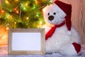 New Year`s, Christmas bear sitting under a fir tree with a wooden frame mockups for a photo or text. Royalty Free Stock Photo