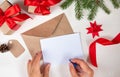 New Year`s composition. Female hands are writing a wish on a blank sheet of paper. Gifts, red ribbon and an envelope from eco