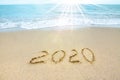 New Year 2020 on the sandy shore against the backdrop of sea waves. Beautiful sunrays illuminate the inscription 2020 on the sand Royalty Free Stock Photo