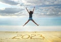 New Year 2023 written on sand, happy girl with hands up jumping on beach