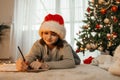 New Year& x27;s and Christmas. A teenage girl in a santa claus hat writes a letter to Santa Claus next to a decorated