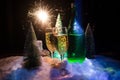 New Years Eve celebration background with pair of flutes and bottle of champagne with christmas tree on snow on dark background. Royalty Free Stock Photo