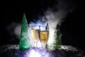 New Years Eve celebration background with pair of flutes and bottle of champagne with christmas tree on snow on dark background. Royalty Free Stock Photo