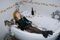 New Years Party Birthday celebration. Happy young woman in evening dress sitting in the bathtub drinking champagne and