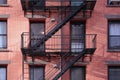 New York City apartment building painted red brick exterior, windows, and diagonal fire escape stairs Royalty Free Stock Photo