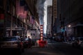 New York City street view. Busy life, people, stores, American flags, cars and the white-orange striped steam vent in the middle