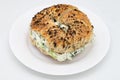 New York City Style Toasted Everything Bagel filled with Scallion Cream Cheese on a White Plate Royalty Free Stock Photo