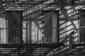 New York City tenement style apartment building windows with fire escape casting long shadows in early morning sunlight Royalty Free Stock Photo