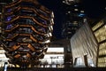 Vessel TKA, a spiral endless staircase with the Shed near it, skyscrappers behind. Night view with bright lights. Hudson Yards