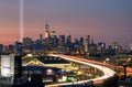 The 9/11 tribute lights seen next to One World Trade at sunset. Car light trails from Interstate 278 I-278 heading towards Manha