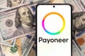 smartphone screen with digital payment service Payoneer mobile application on US dollar banknotes background