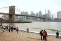 New York, USA - december 26, 2019: Tourists walking on riverside of East River and admiring of famous Brooklyn Bridge and Royalty Free Stock Photo