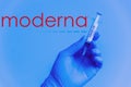 New york, USA - 5 january 2021: moderna covid vaccine in hand, closeup of syringe on blue background with face mask. concept of