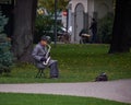 New York, USA - July, 2017: old man in a raincoat and a hat plaing saxophone in a park