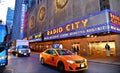 New York USA, urban classic building, colors and neon lights of Radio City Music Hall in Manhattan with urban traffic and yellow t Royalty Free Stock Photo