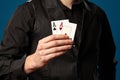 Newbie in poker, in black vest and shirt. Holding two playing cards while posing against blue studio background