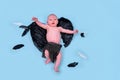 A newborn baby boy with black evil wings on a blue studio background, copy space. An infant caucasian child in a diaper aged one