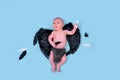 A newborn baby boy with dark demon wings on a blue studio background, copy space. An infant caucasian child in a diaper aged one