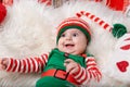 Newborn baby girl dressed in gnome costume lying on white fur carpet among christmas decorations. Royalty Free Stock Photo