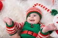 Newborn baby girl dressed in gnome costume lying on white fur carpet among christmas decorations. Royalty Free Stock Photo