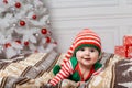 Newborn baby girl dressed in gnome costume lying on white fur carpet among christmas decorations. Royalty Free Stock Photo