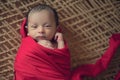 Newborn baby boy waking up,squinting and opening his eyes, wrapped in red cloth 1 month old baby on latticework half eyes open Royalty Free Stock Photo