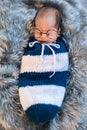 Newborn baby boy wearing glasses sleeping and swaddled in a knit wrap on bed Royalty Free Stock Photo